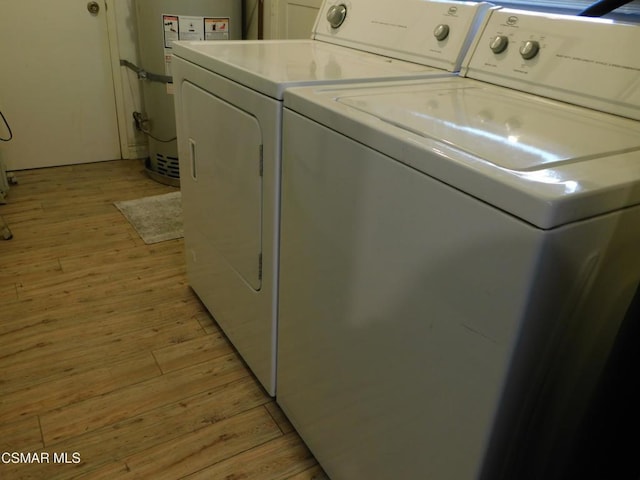 washroom with washing machine and dryer, water heater, and light hardwood / wood-style floors