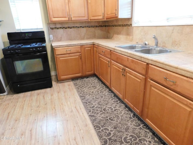 kitchen featuring tile countertops, light hardwood / wood-style floors, tasteful backsplash, black range with gas cooktop, and sink