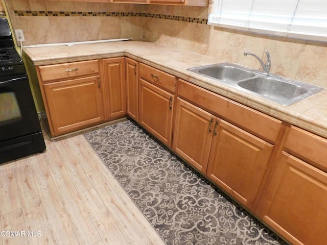 kitchen featuring tile counters, decorative backsplash, light wood-type flooring, black range with electric cooktop, and sink