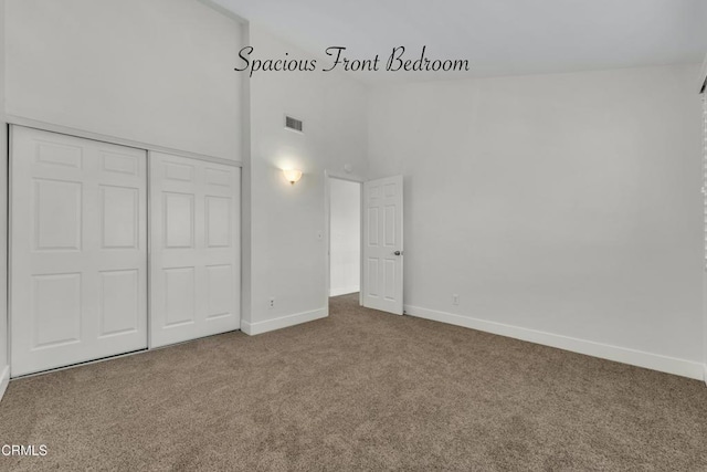 unfurnished bedroom featuring a closet, high vaulted ceiling, and carpet flooring