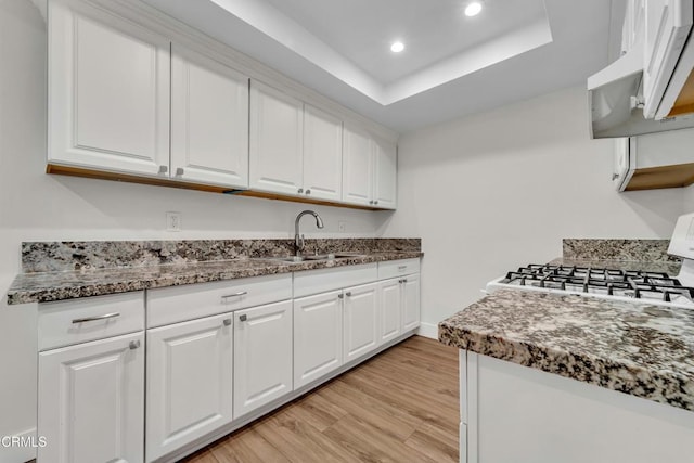 kitchen featuring sink, white cabinetry, a tray ceiling, and light hardwood / wood-style flooring