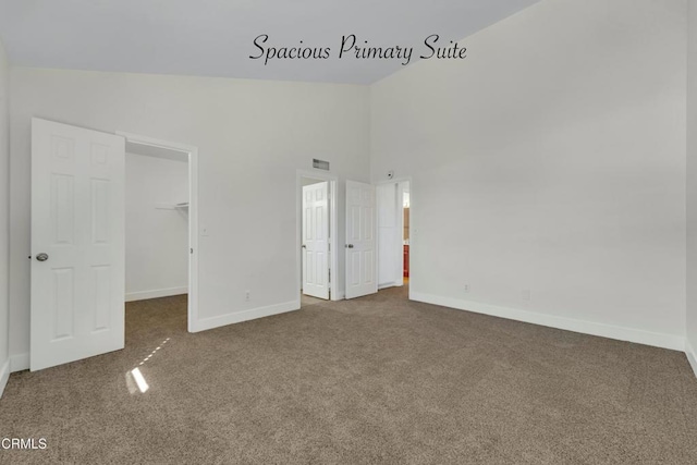 unfurnished bedroom featuring carpet flooring, a closet, high vaulted ceiling, and a walk in closet