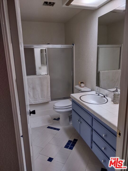 full bathroom with toilet, bath / shower combo with glass door, tile patterned flooring, and vanity