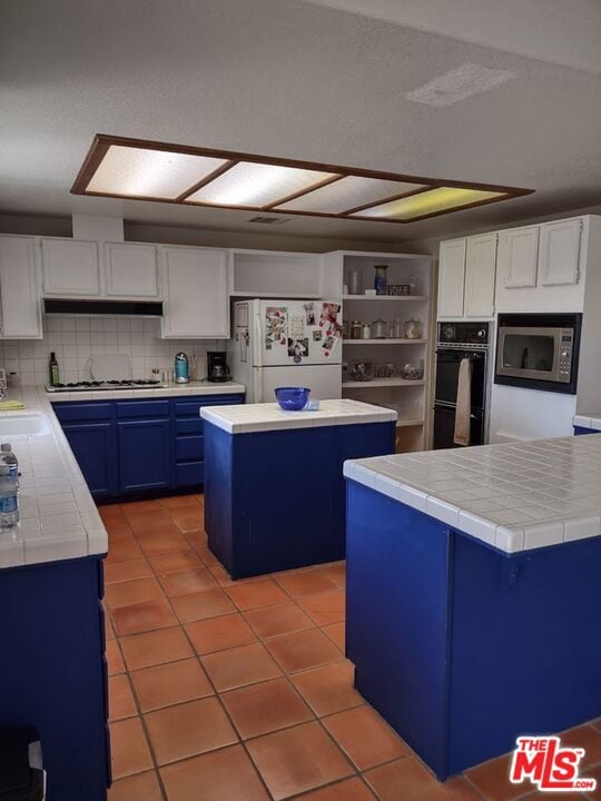 kitchen featuring tile counters, a kitchen island, white cabinetry, stainless steel appliances, and blue cabinets