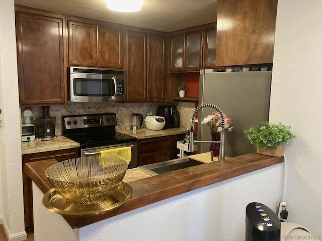 kitchen with appliances with stainless steel finishes, dark brown cabinets, tasteful backsplash, and sink