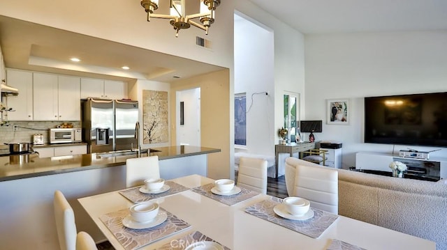 dining space with sink, an inviting chandelier, a high ceiling, and a raised ceiling