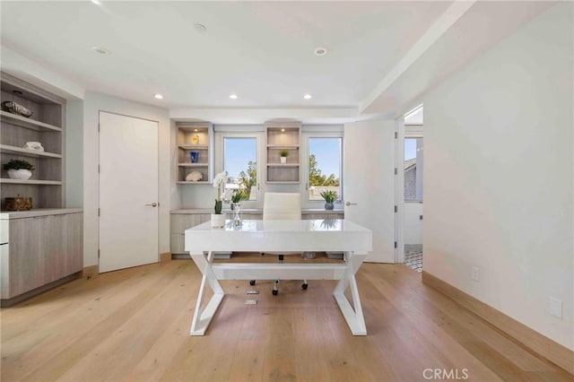 office with built in shelves and light hardwood / wood-style flooring