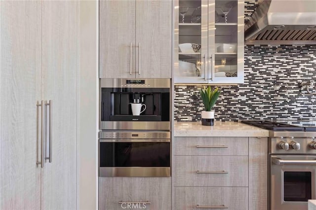 kitchen with wall chimney range hood, appliances with stainless steel finishes, light brown cabinets, and tasteful backsplash