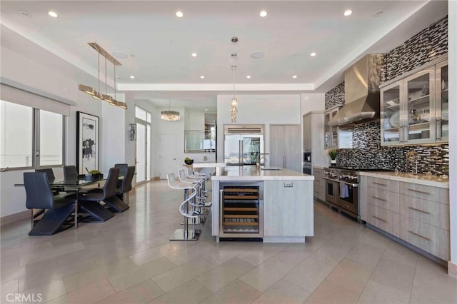 kitchen with a large island with sink, pendant lighting, premium appliances, wall chimney exhaust hood, and beverage cooler