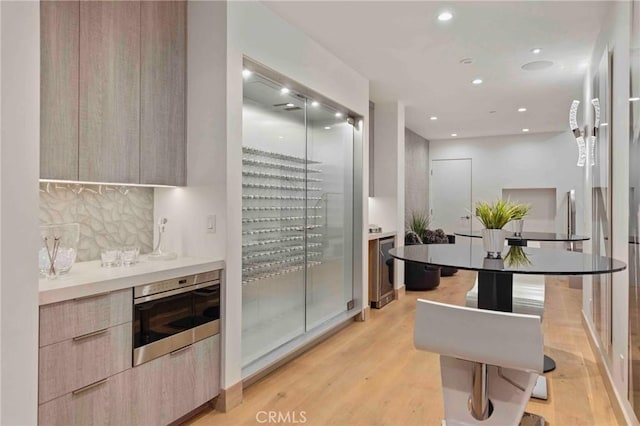 kitchen featuring tasteful backsplash, light wood-type flooring, light brown cabinets, and wall oven