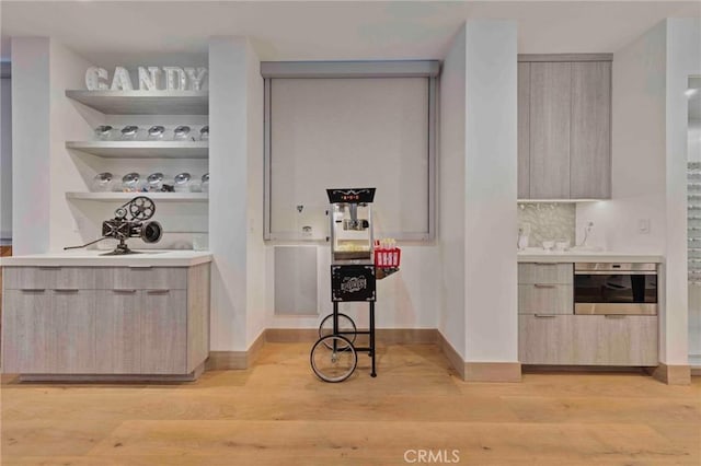 bar featuring decorative backsplash, stainless steel oven, light hardwood / wood-style floors, and light brown cabinets