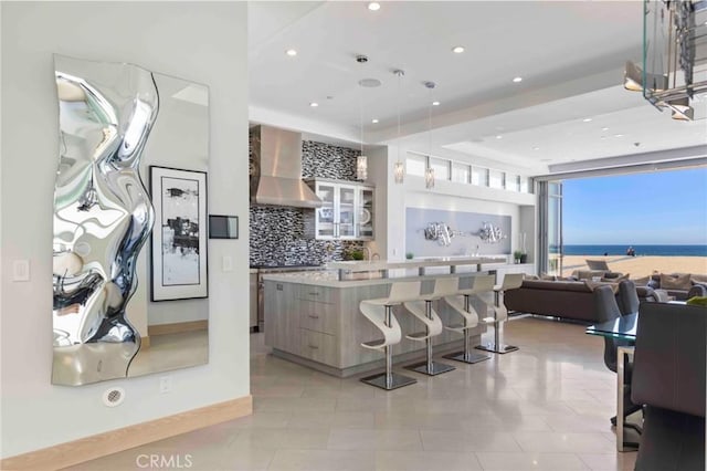 kitchen with decorative light fixtures, backsplash, wall chimney range hood, a center island, and a water view