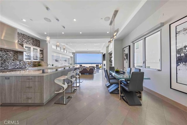 kitchen featuring a breakfast bar area, plenty of natural light, backsplash, decorative light fixtures, and wall chimney exhaust hood