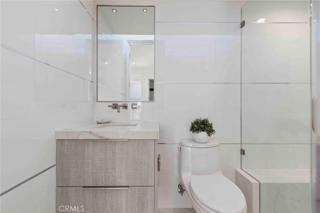 bathroom featuring a shower with door, tile walls, toilet, and vanity