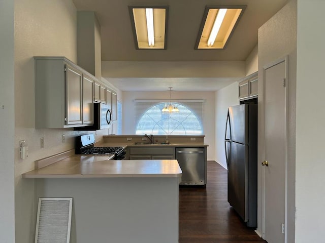 kitchen featuring decorative light fixtures, sink, kitchen peninsula, stainless steel appliances, and dark wood-type flooring