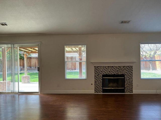 unfurnished living room featuring dark wood-type flooring, a tile fireplace, and a textured ceiling