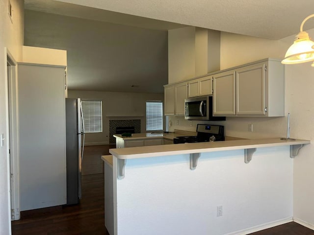 kitchen with dark hardwood / wood-style flooring, stainless steel appliances, a kitchen bar, a tiled fireplace, and kitchen peninsula