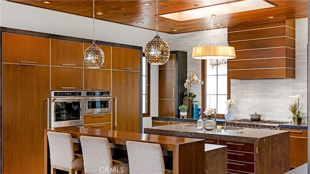 kitchen with wood ceiling, appliances with stainless steel finishes, a kitchen island with sink, hanging light fixtures, and backsplash