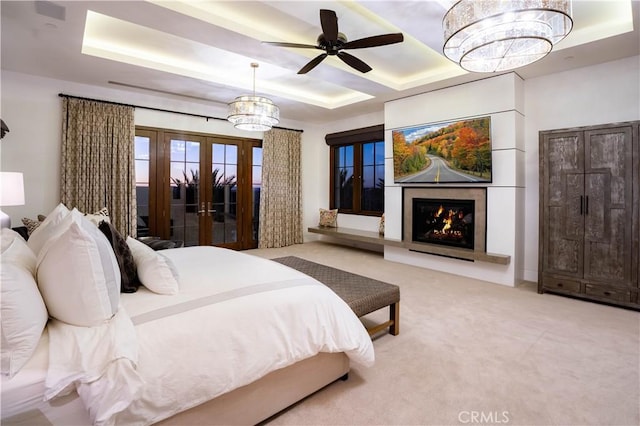bedroom with a tray ceiling, french doors, a premium fireplace, carpet floors, and a chandelier