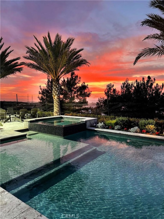 pool at dusk with a patio area and an in ground hot tub