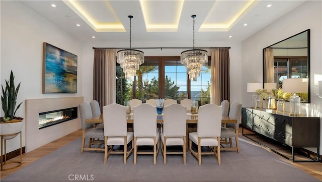 dining area with a chandelier, a raised ceiling, wood finished floors, and a glass covered fireplace