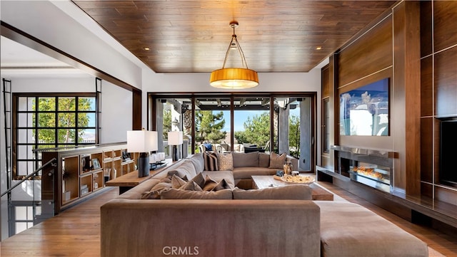 living area featuring a glass covered fireplace, wood finished floors, a wealth of natural light, and wood ceiling