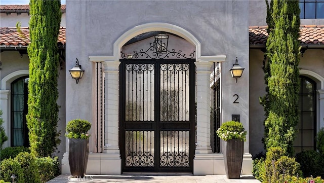 entrance to property with a tiled roof, a gate, and stucco siding