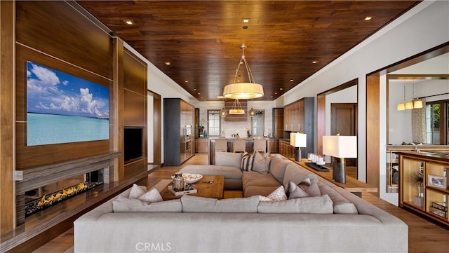 living room with wood finished floors, wood ceiling, ornamental molding, and a lit fireplace