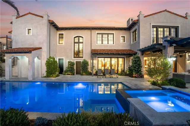 back house at dusk featuring a pool with hot tub and a patio