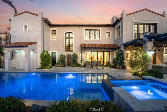 back of property at dusk with stucco siding, a pergola, a patio area, and french doors