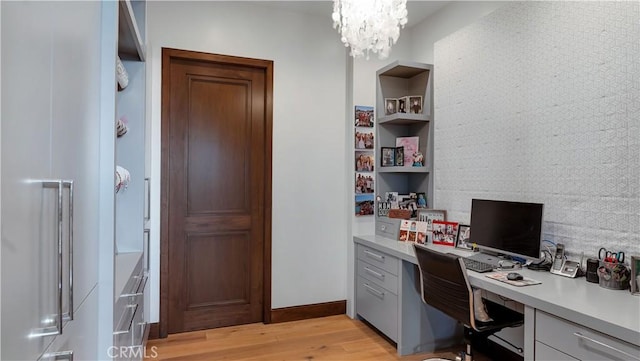 office area featuring built in study area, baseboards, a notable chandelier, and light wood-style flooring