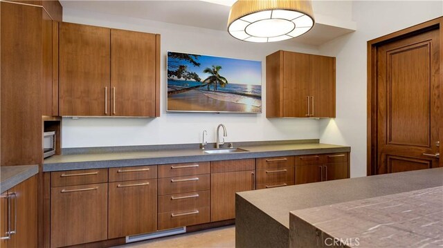 kitchen with brown cabinetry, dark countertops, a sink, and visible vents