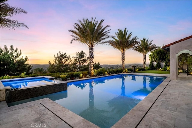 pool at dusk with a pool with connected hot tub and a patio