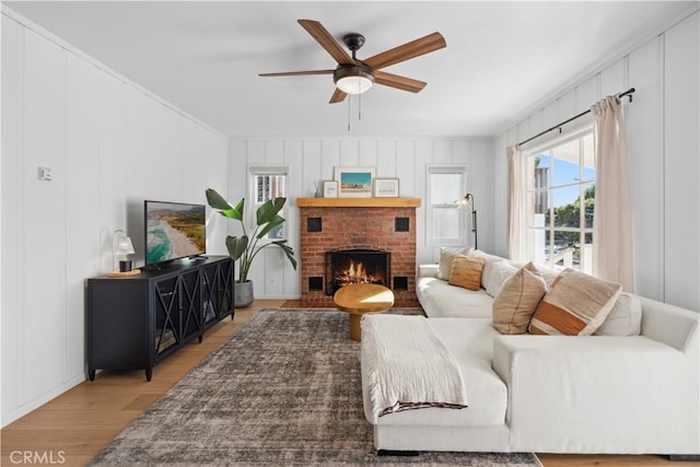 living room featuring ceiling fan, wood-type flooring, and a brick fireplace