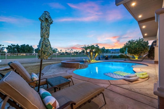 pool at dusk with a patio and an in ground hot tub