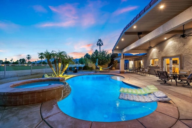 pool at dusk featuring an in ground hot tub, a patio, ceiling fan, and french doors