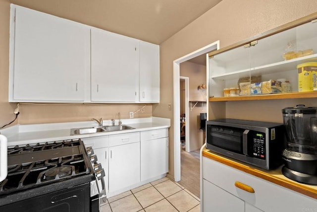 kitchen featuring light tile patterned flooring, black gas range oven, sink, and white cabinets