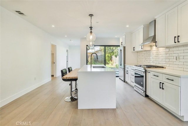 kitchen with a center island with sink, wall chimney range hood, white cabinetry, appliances with stainless steel finishes, and sink