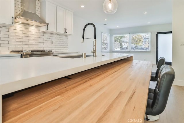 kitchen with hanging light fixtures, wall chimney range hood, light hardwood / wood-style floors, tasteful backsplash, and white cabinets