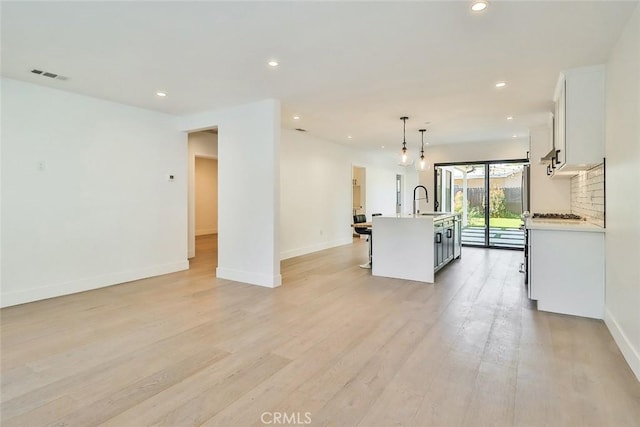 kitchen with sink, decorative light fixtures, white cabinets, light hardwood / wood-style floors, and a center island with sink