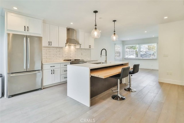 kitchen featuring stainless steel fridge, white cabinetry, wall chimney range hood, and a center island with sink