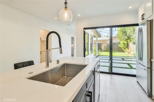 kitchen featuring sink, white cabinetry, stainless steel fridge, and hanging light fixtures