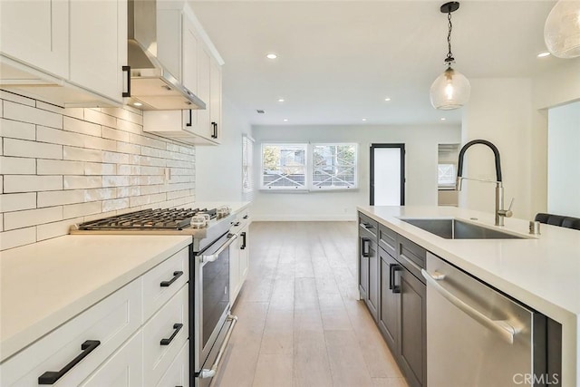 kitchen featuring sink, white cabinetry, wall chimney exhaust hood, hanging light fixtures, and appliances with stainless steel finishes