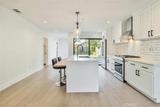 kitchen with a kitchen island with sink, appliances with stainless steel finishes, white cabinets, wall chimney range hood, and sink