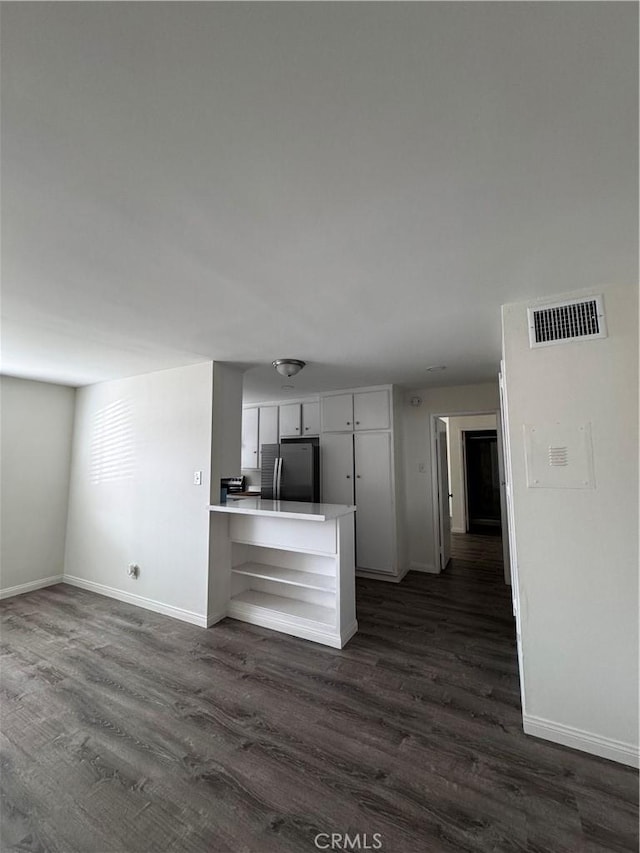 kitchen with kitchen peninsula, dark hardwood / wood-style floors, stainless steel refrigerator, and white cabinetry