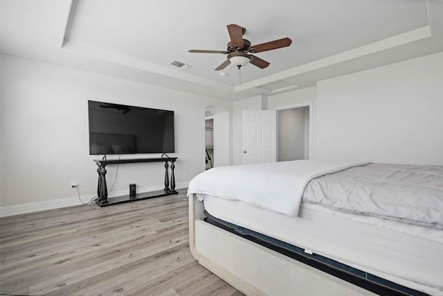 bedroom featuring a raised ceiling, ceiling fan, and light hardwood / wood-style flooring