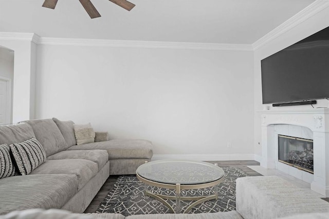 living room with ceiling fan, wood-type flooring, a tile fireplace, and crown molding