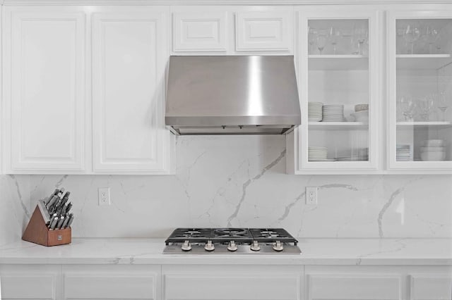 kitchen with stainless steel gas cooktop, decorative backsplash, light stone countertops, and wall chimney range hood