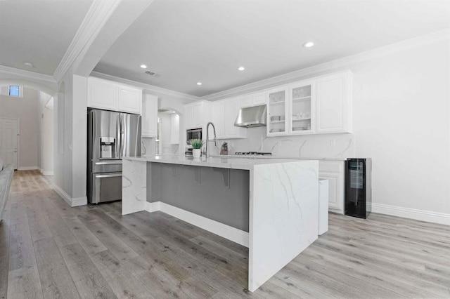 kitchen with exhaust hood, stainless steel refrigerator with ice dispenser, white cabinetry, an island with sink, and ornamental molding