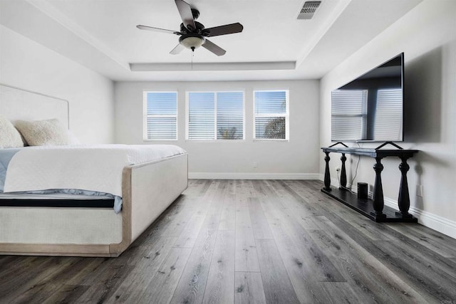 bedroom featuring ceiling fan, multiple windows, hardwood / wood-style flooring, and a raised ceiling